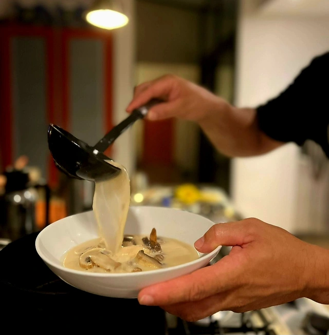 Chef Eddie ladling creamy mushroom soup into a bowl in the kitchen
